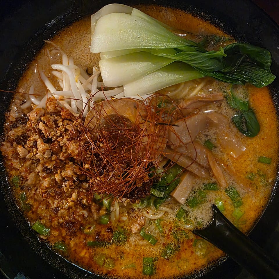 A close-up of a bowl of Yatai Ramen with bok choy, bean sprouts, ground meat, and chili threads.