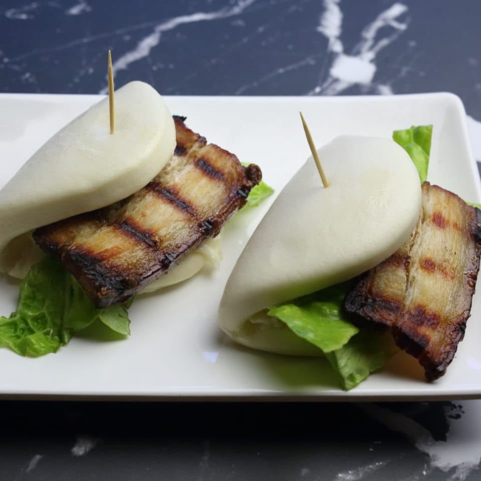 Two Yatai Ramen pork belly bao buns with lettuce on a white rectangular plate.