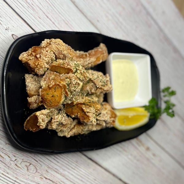 Crispy fried chicken pieces with a side of creamy sauce, lemon, and parsley on a black plate.