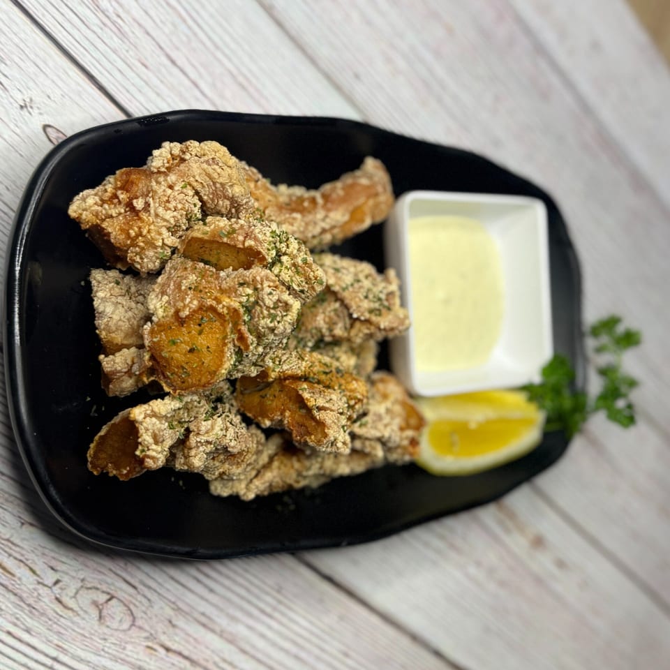 Crispy fried chicken pieces with a side of creamy sauce, lemon, and parsley on a black plate.