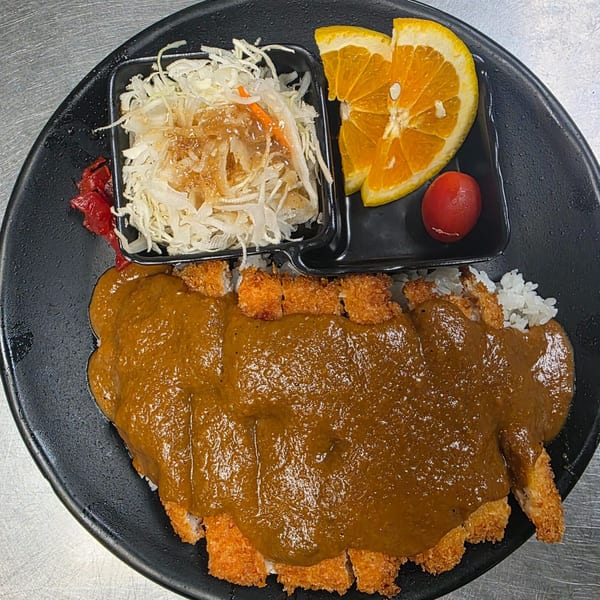 Yatai Ramen's Japanese curry katsu with rice, shredded cabbage salad, orange slices, and a cherry tomato.
