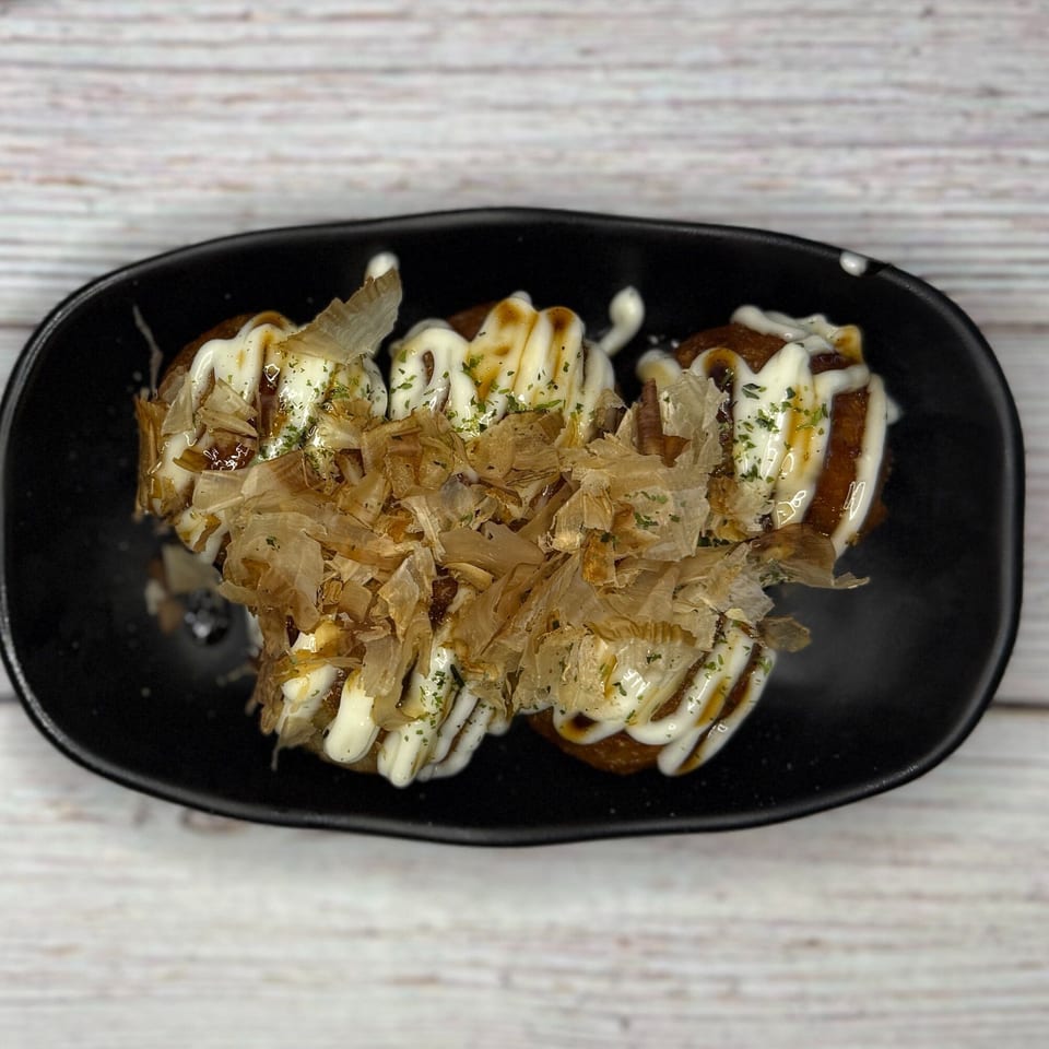 Three takoyaki balls topped with white sauce, brown sauce, dried bonito flakes, and green herbs.