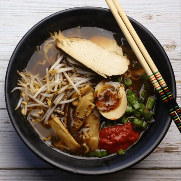 A bowl of Yatai Ramen with chicken, bean sprouts, egg, bamboo shoots, and chili paste.