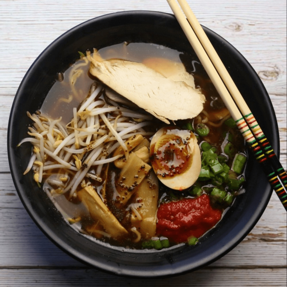 A bowl of Yatai Ramen with chicken, bean sprouts, egg, bamboo shoots, and chili paste.