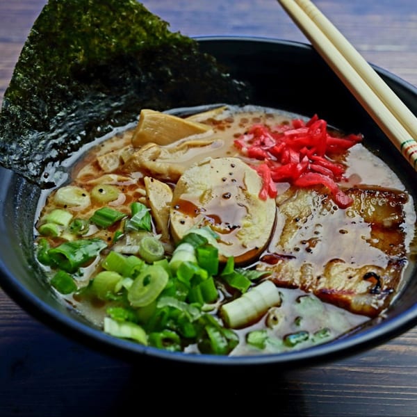 A bowl of Yatai Ramen with pork, egg, green onions, red ginger, and nori, with chopsticks.