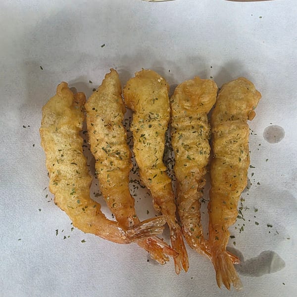 Five golden-brown tempura shrimp, lightly seasoned with herbs, on white parchment paper.