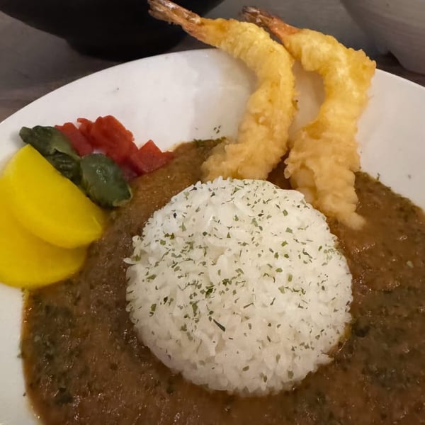 Japanese curry with a mound of white rice, two pieces of tempura shrimp, and pickled vegetables.